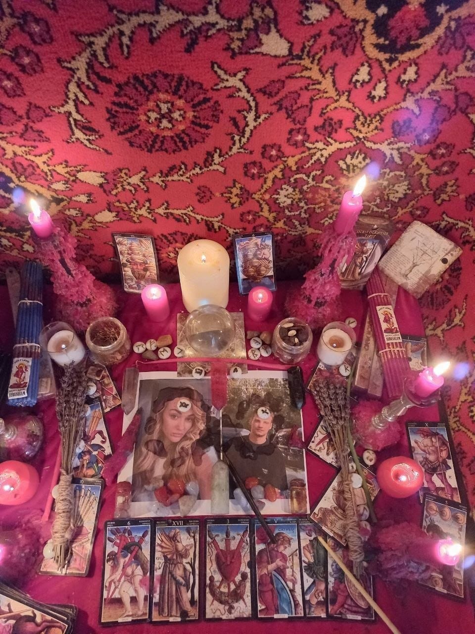 Altar de amarre de pareja: fotos de los dos unidas en el centro, runas colocadas sobre las fotos, velas rosas encendidas, lavanda, esfera de cristal y cartas del tarot