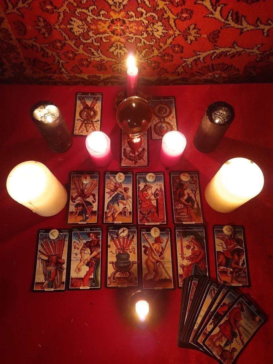 Mesa de trabajo para el estudio del caso: cartas dispuestas sobre mantel rojo, velas encendidas, esfera de cristal y velas negras de protección